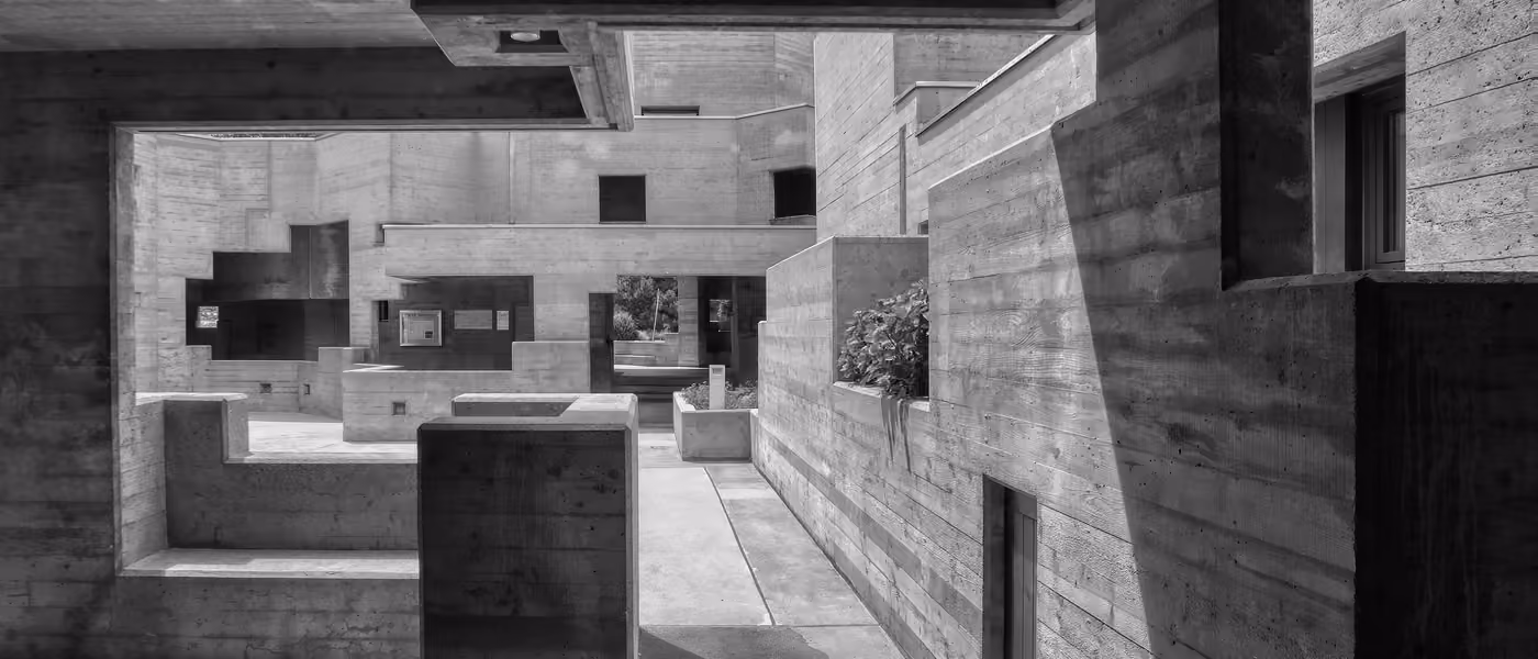 Hard midday light carves deep shadows across the raw concrete volumes of a brutalist church courtyard.